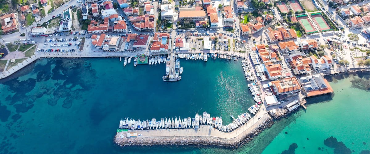 An aerial view of a coastal town with a marina, boats, and buildings.