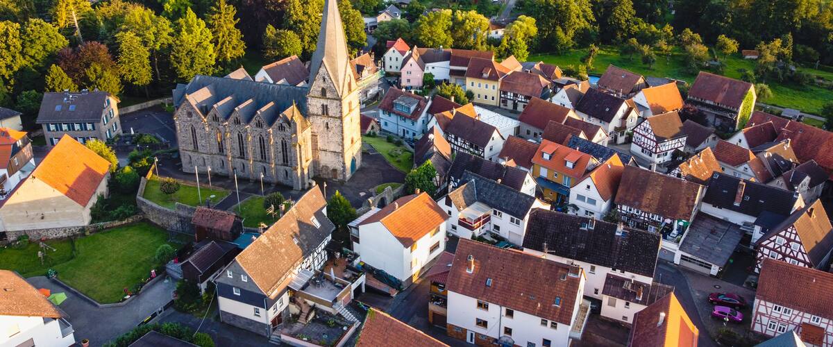 An aerial view of a village with a prominent church, surrounded by traditional houses and green fields.