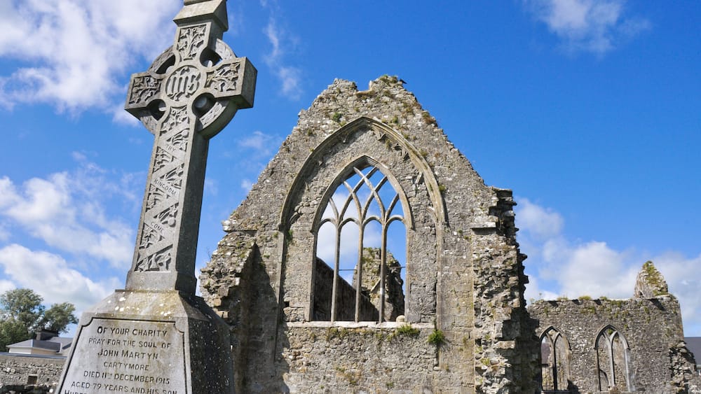 A stone cross with inscriptions and a ruined church with arched windows.