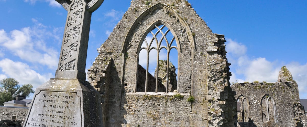 A stone cross with inscriptions and a ruined church with arched windows.