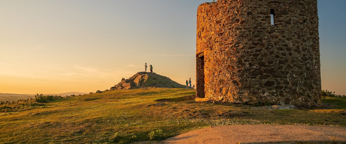 A stone tower and a hill with people on top.
