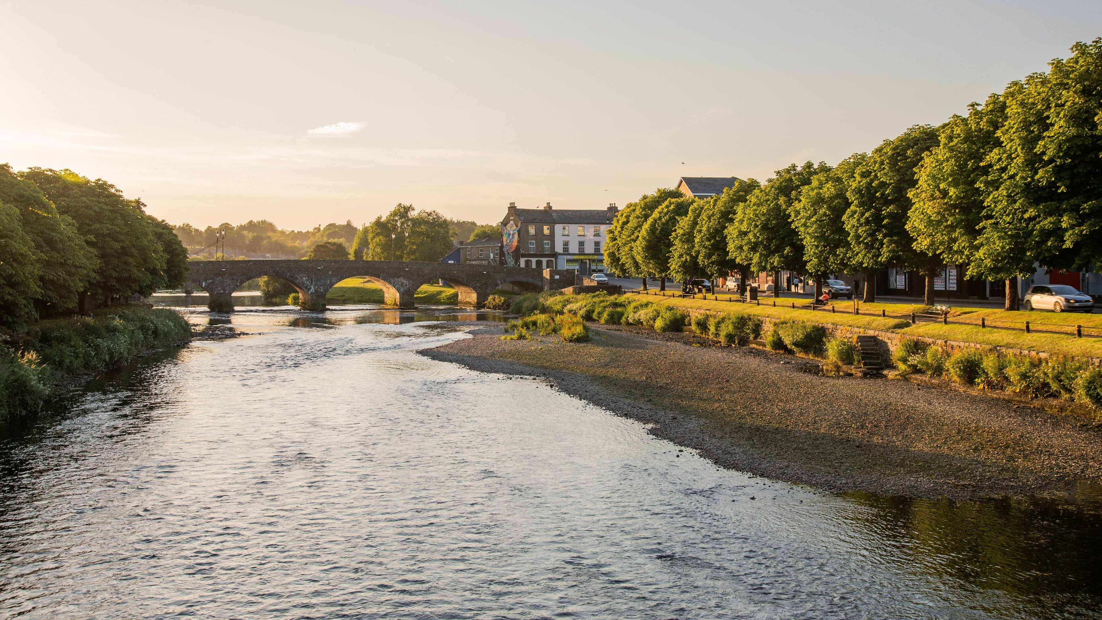 A river with a stone bridge, trees, and buildings along the banks.