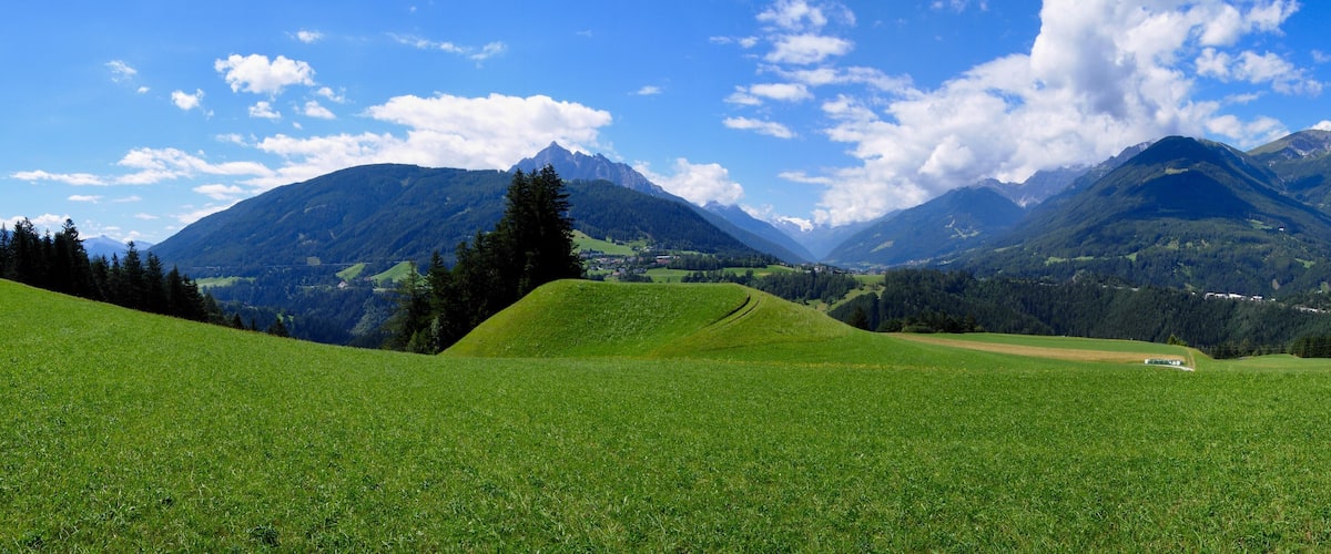 A green field with a bridge and mountains in the background.