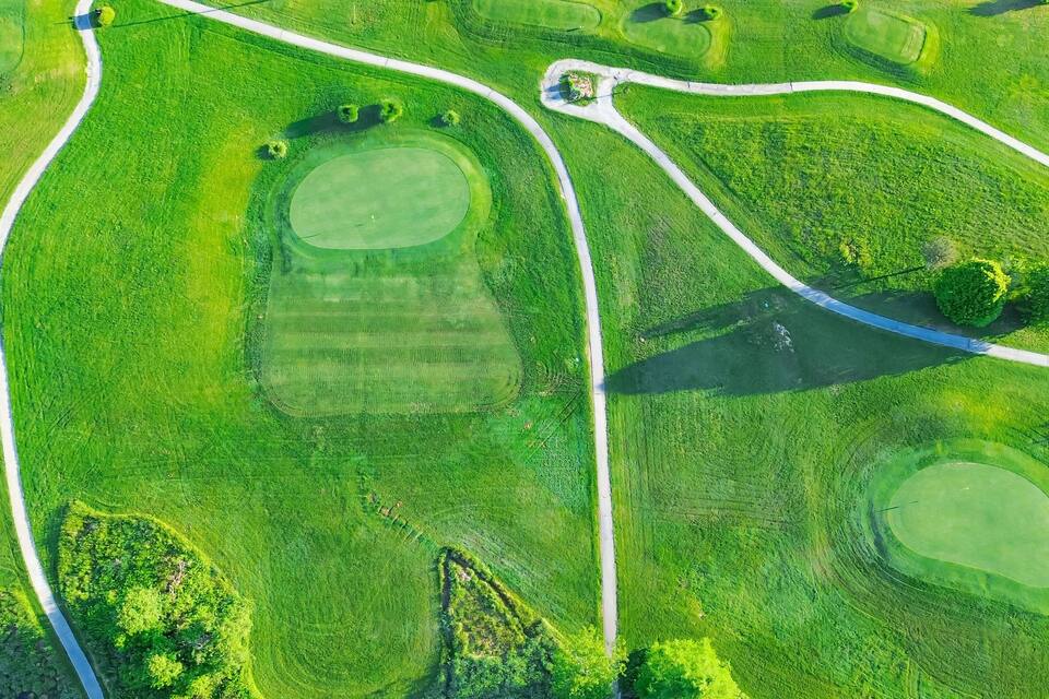 An aerial view of a golf course with multiple greens, fairways, and a winding path.