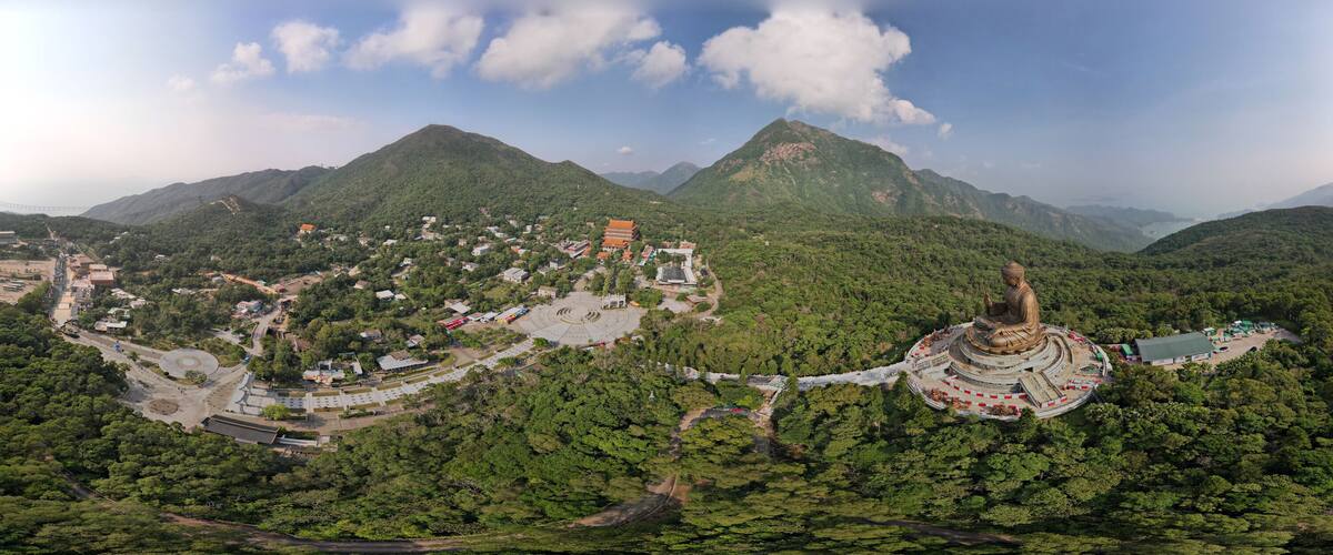 Un paisaje montañoso con una gran estatua de Buda, un complejo de templos y un puente al fondo.