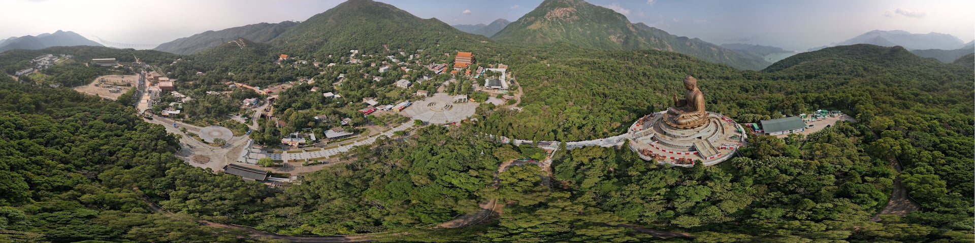 A mountainous landscape with a large Buddha statue, a temple complex, and a bridge in the background.