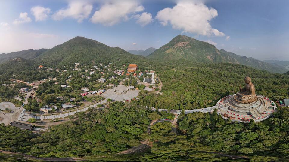 A mountainous landscape with a large Buddha statue, a temple complex, and a bridge in the background.