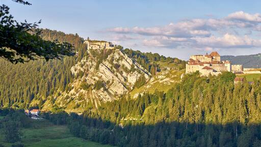 Un château perché sur une colline, entouré d’une forêt dense et de montagnes.