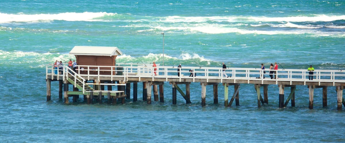 A pier extending into the ocean with people fishing and a small building at the end.