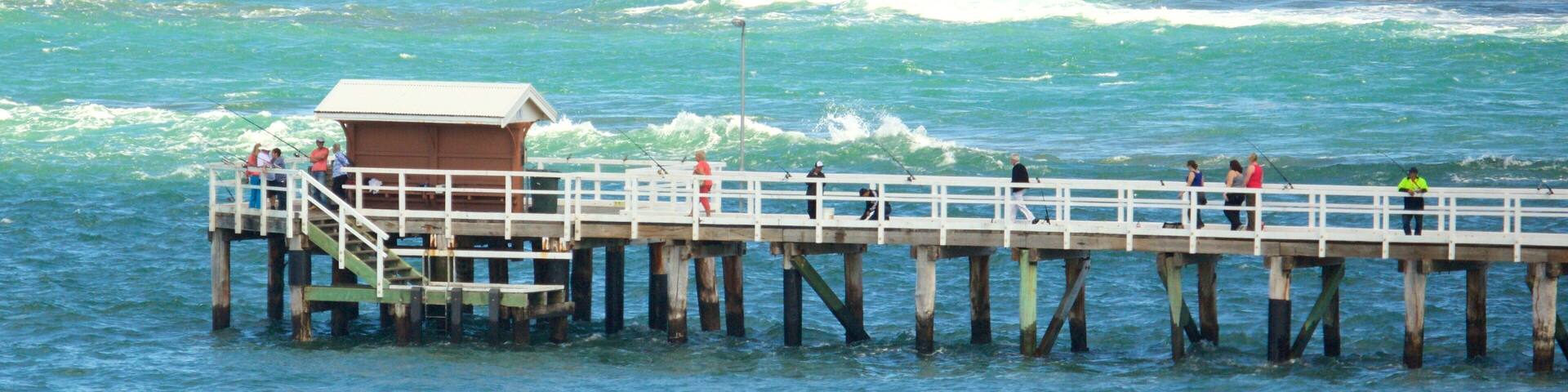 A pier extending into the ocean with people fishing and a small building at the end.
