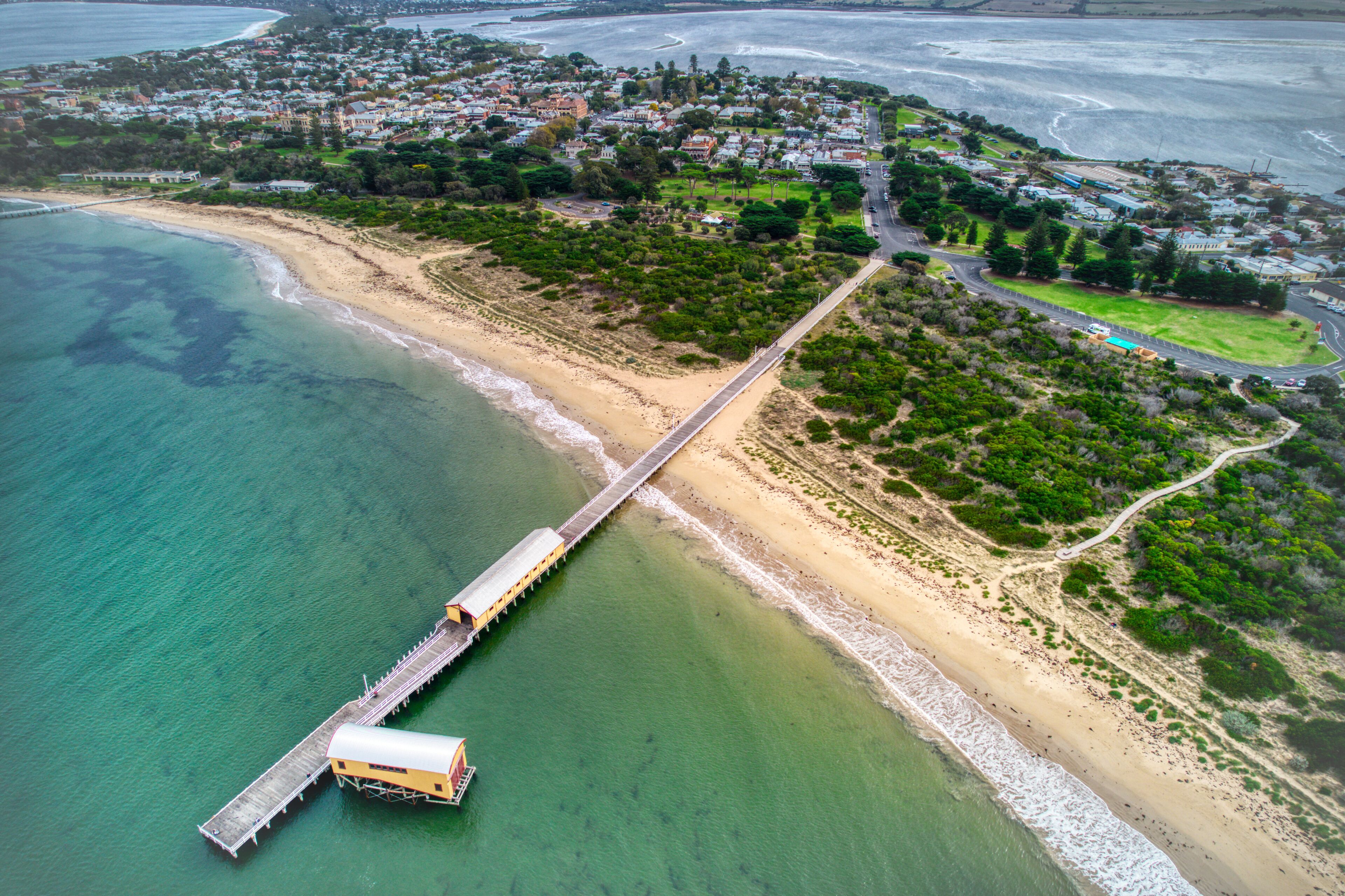A coastal town with a long pier extending into the ocean, surrounded by residential areas and greenery.