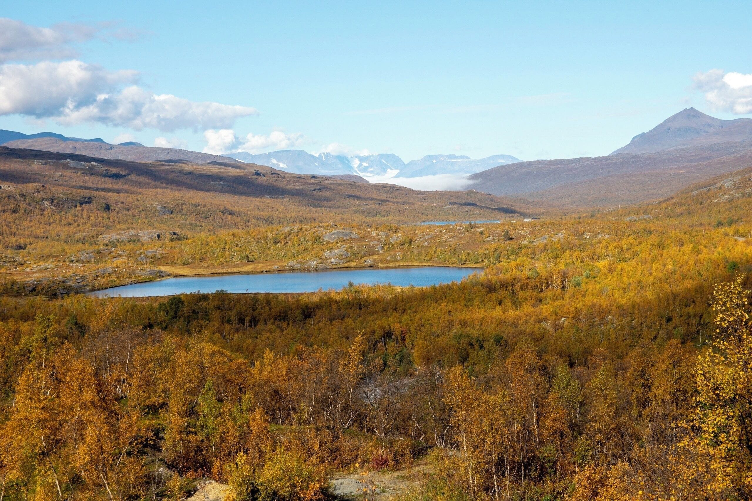 Un lago rodeado por un bosque de colores otoñales y montañas distantes.