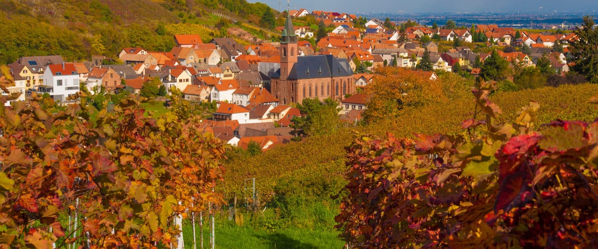 A town with red-roofed houses, a prominent church with a tall steeple, and a hillside in the background.