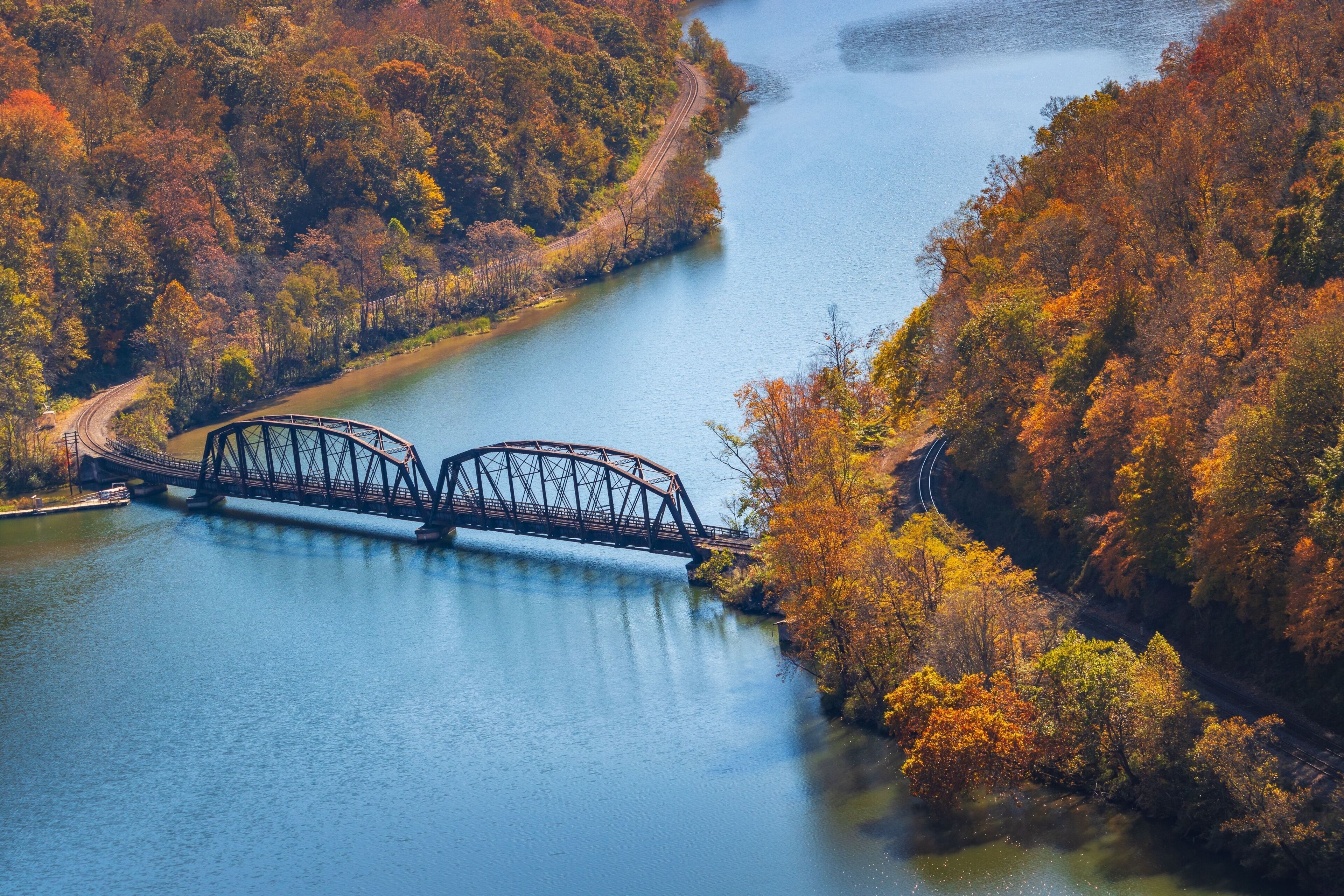 A steel bridge over a river, surrounded by autumn-colored trees.