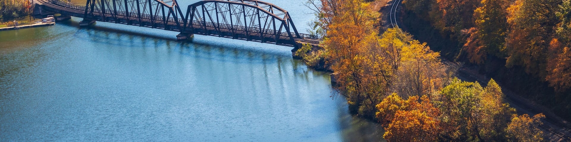 A steel bridge over a river, surrounded by autumn-colored trees.