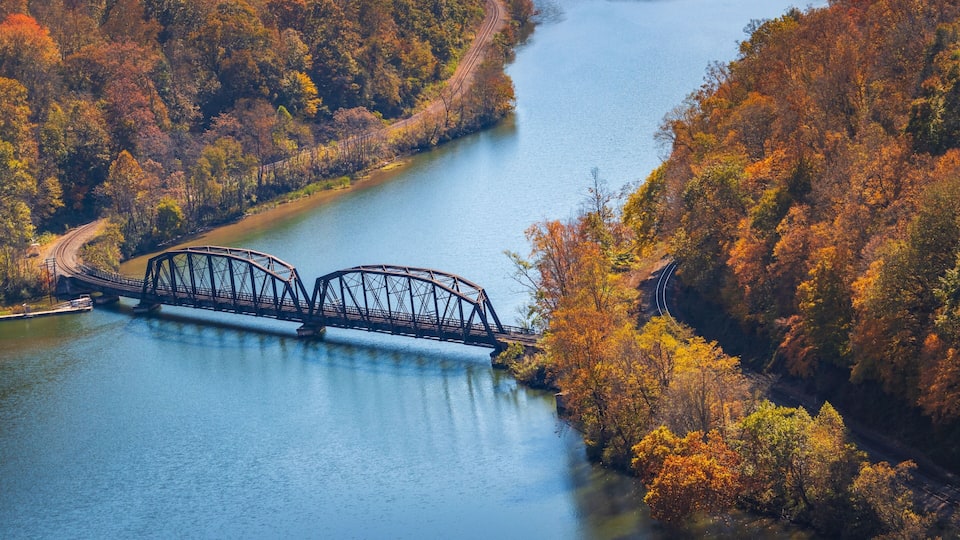 A steel bridge over a river, surrounded by autumn-colored trees.