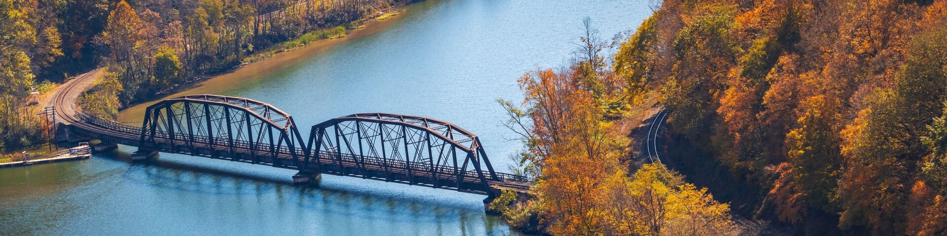 Un puente de acero sobre un río, rodeado de árboles de colores otoñales.