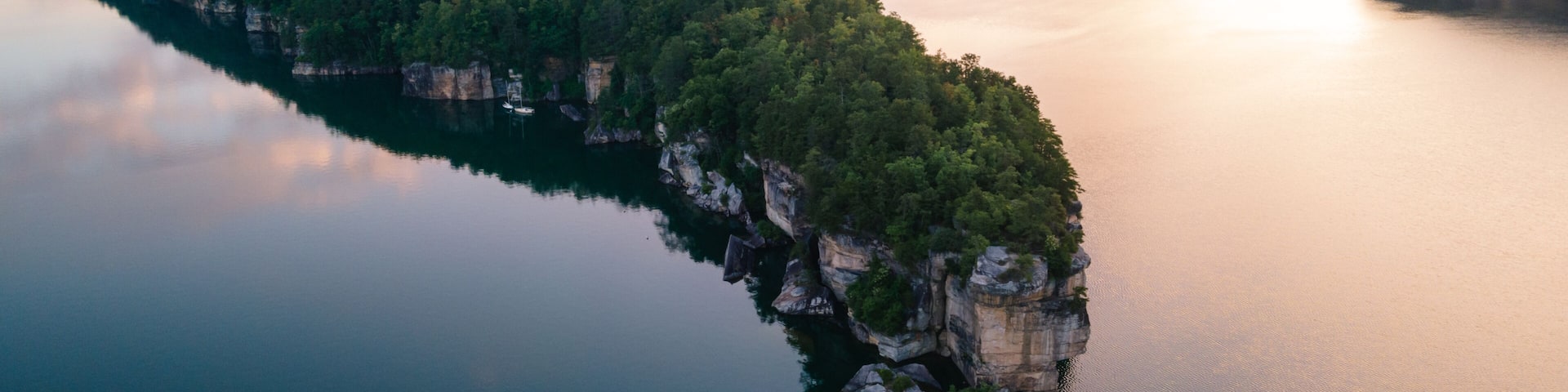 A river winding through a forested peninsula with cliffs on one side and a calm lake reflecting the sky.