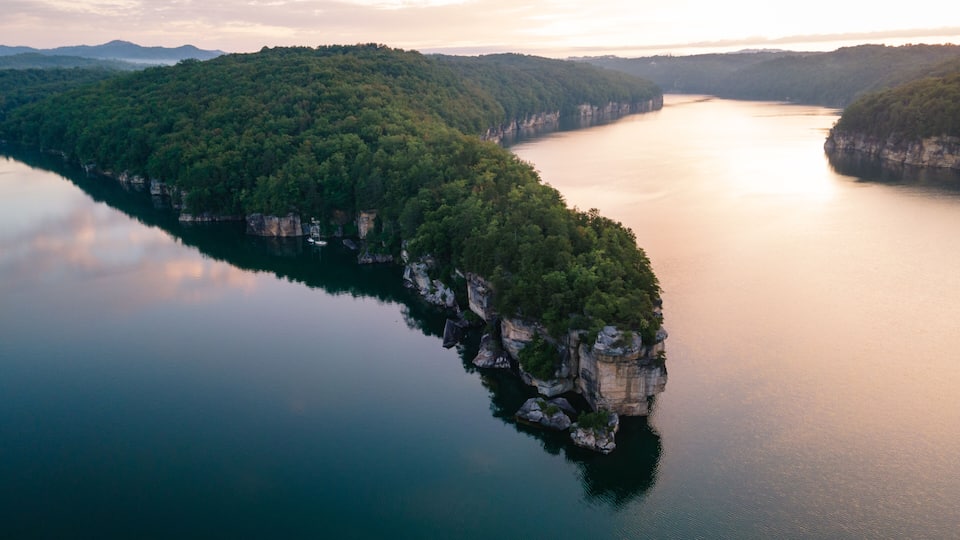 A river winding through a forested peninsula with cliffs on one side and a calm lake reflecting the sky.