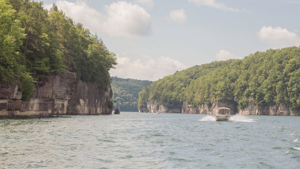 A boat on a calm river surrounded by cliffs and dense greenery.