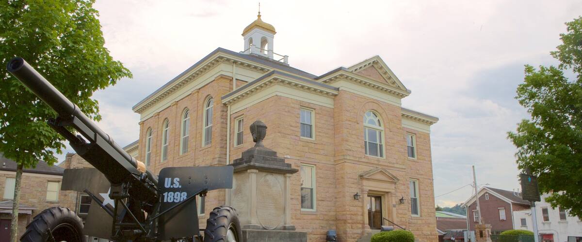 A historical cannon in front of a large brick building with a bell tower.