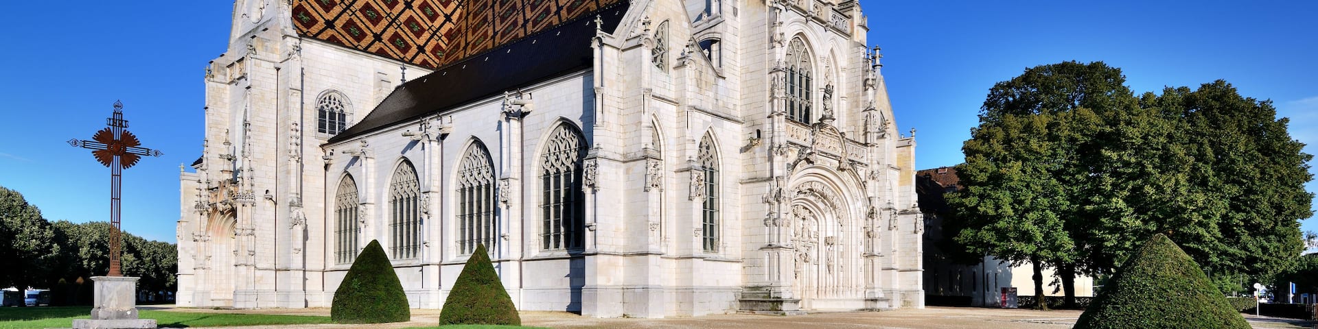 A historic cathedral with a distinctive tiled roof, ornate Gothic architecture, and a well-manicured lawn.