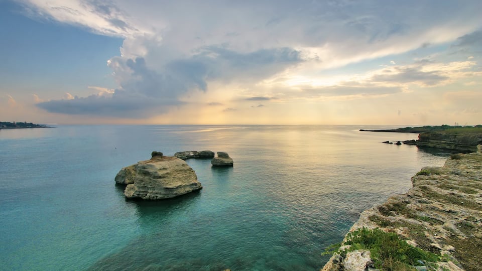 A coastal landscape with clear turquoise waters, rocky formations, and a distant shoreline.