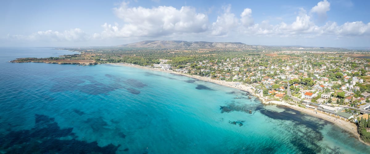 Un pueblo costero con una playa, aguas azul turquesa y montañas al fondo.