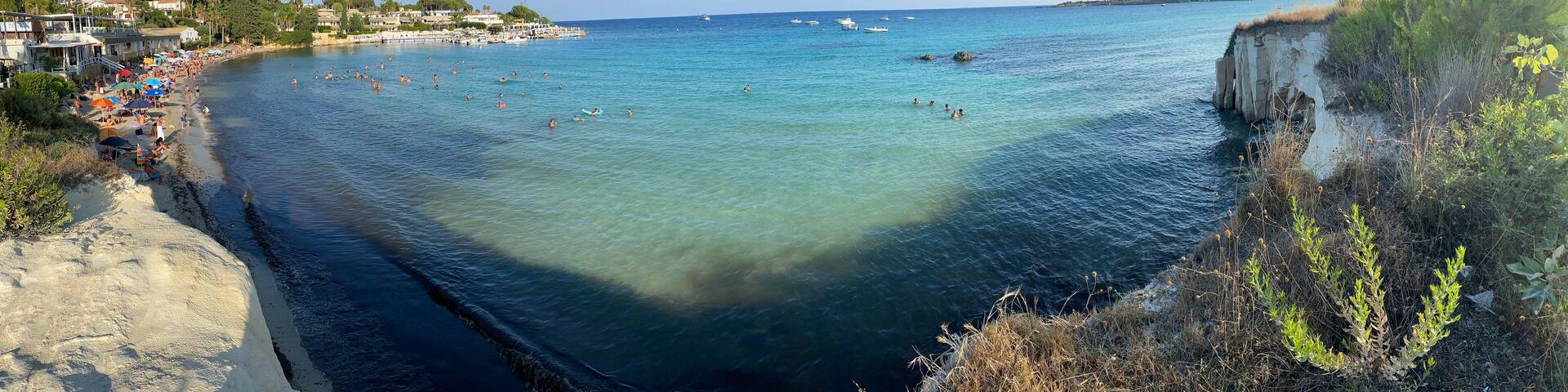 Panoramic view of Fontane Bianche beach, near Syracuse in Sicily, Italy. It is summer and there are many people along the coast.
