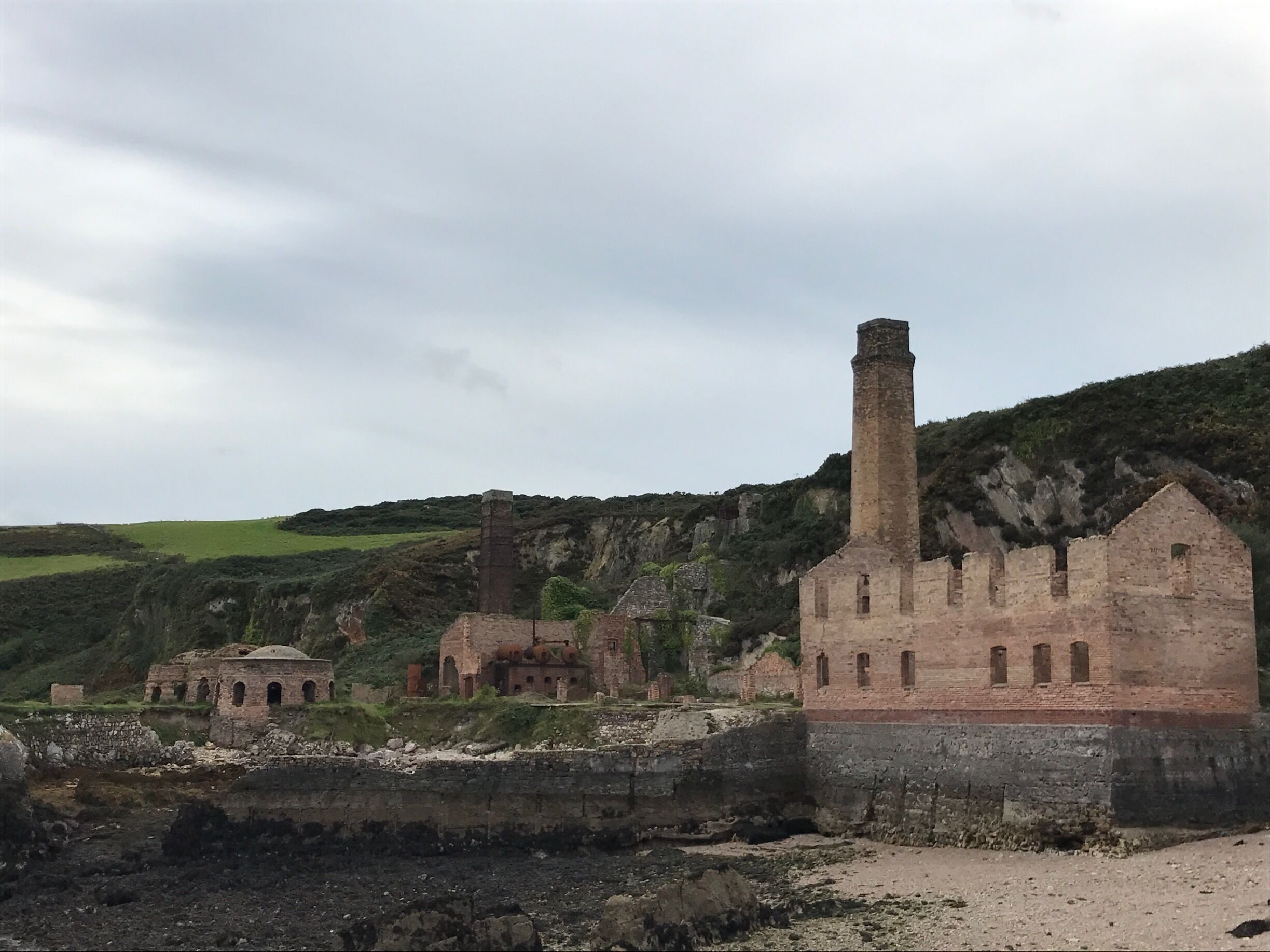 A historical site with ruins, including a tall chimney and several brick buildings.