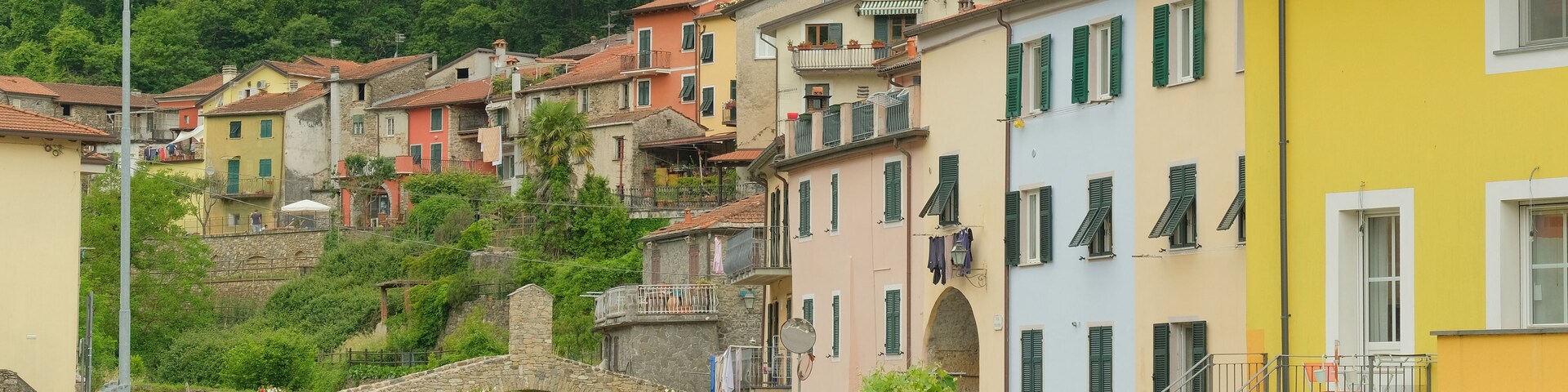 A hillside village with colorful buildings, a stone bridge, and a bell tower.