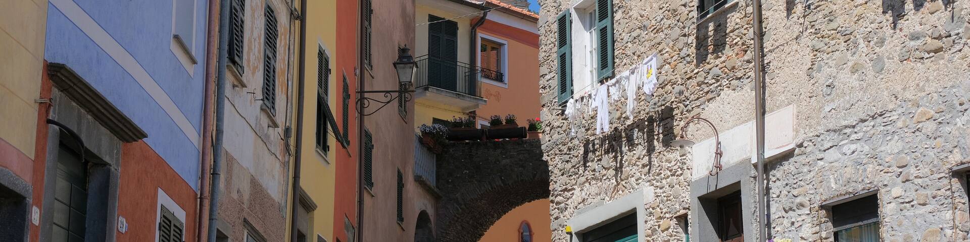 A narrow street with colorful buildings, a stone wall, and a bell tower.