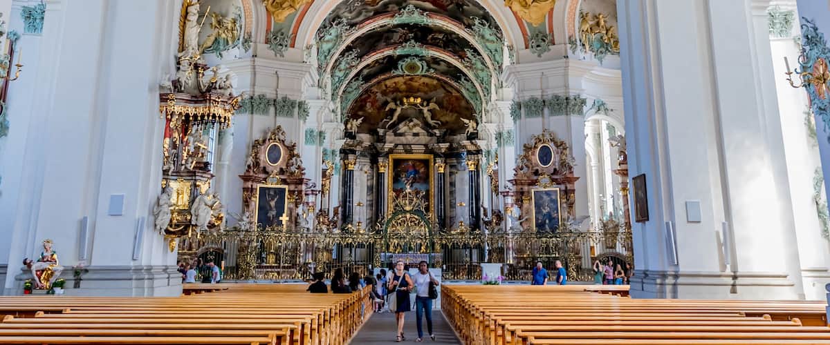 An ornate church interior with a long nave, wooden pews, and elaborate ceiling frescoes.
