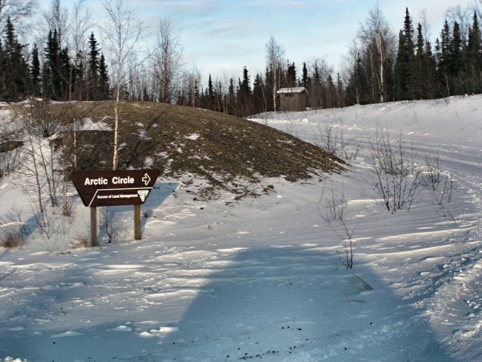 A snow-covered landscape with a sign for the Arctic Circle.