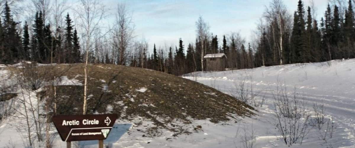 A snow-covered landscape with a sign for the Arctic Circle.