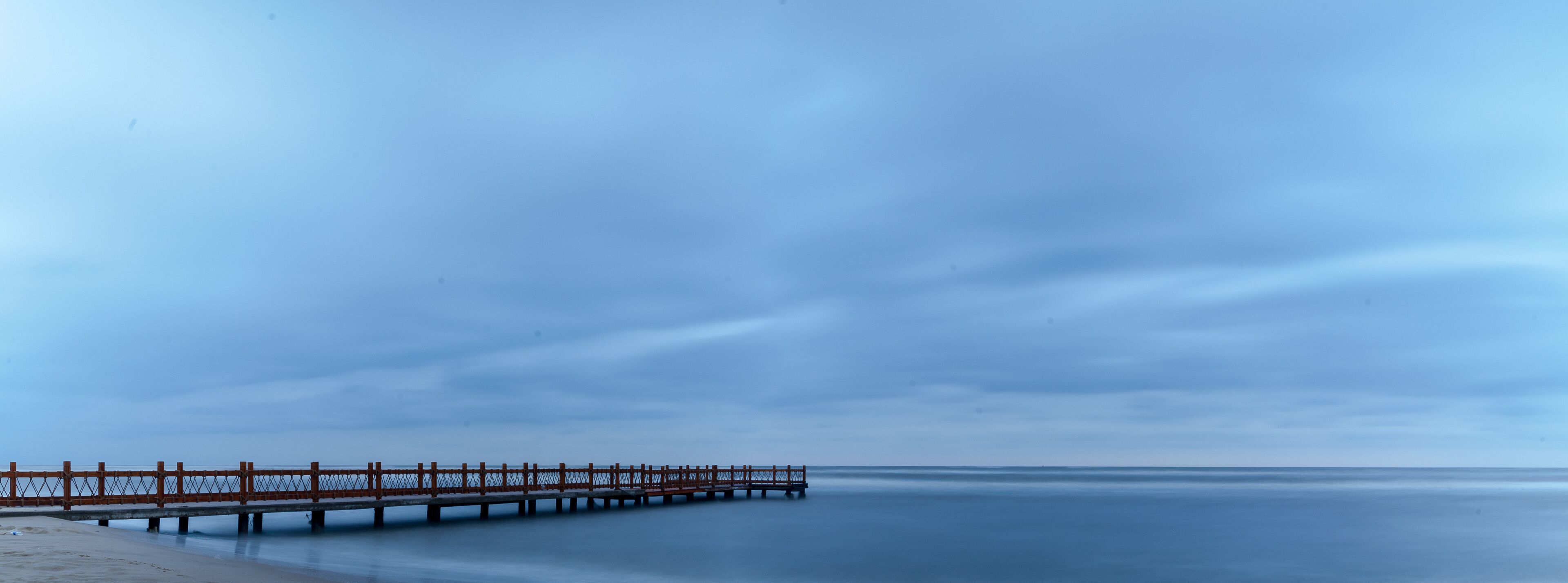 A long pier extending into calm waters under a cloudy sky.