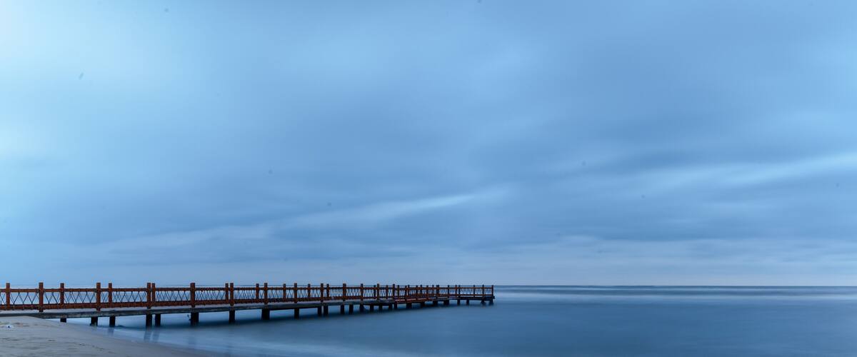A long pier extending into calm waters under a cloudy sky.