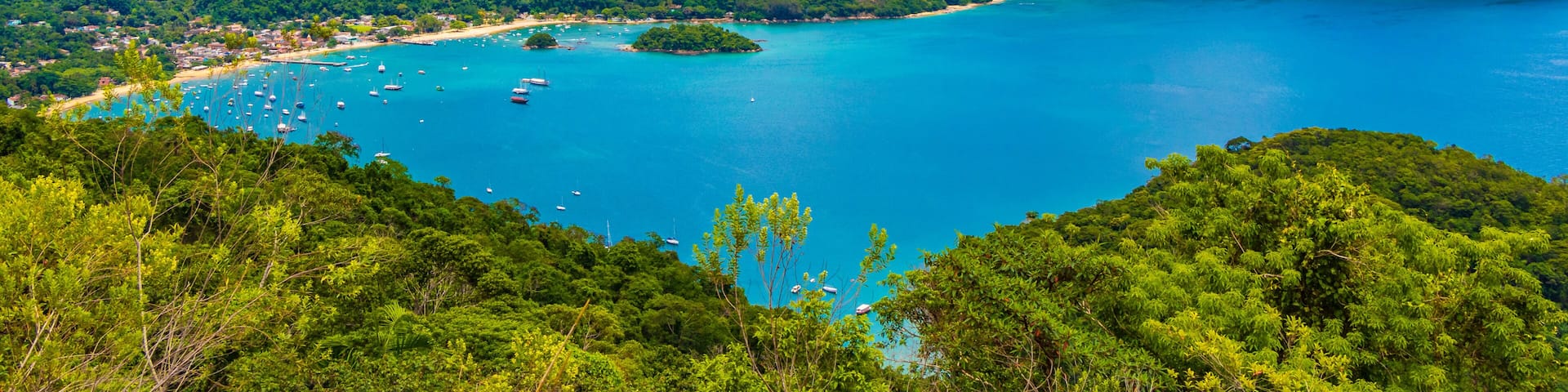 A coastal landscape with a turquoise bay, green hills, and scattered boats.