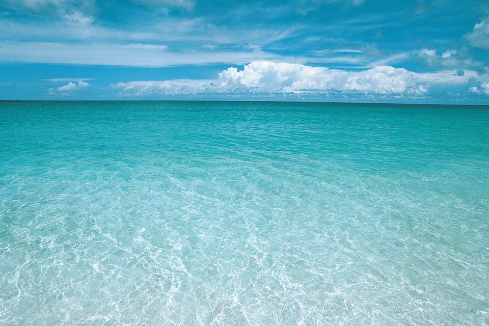 A clear turquoise sea with visible underwater patterns and a partly cloudy sky.