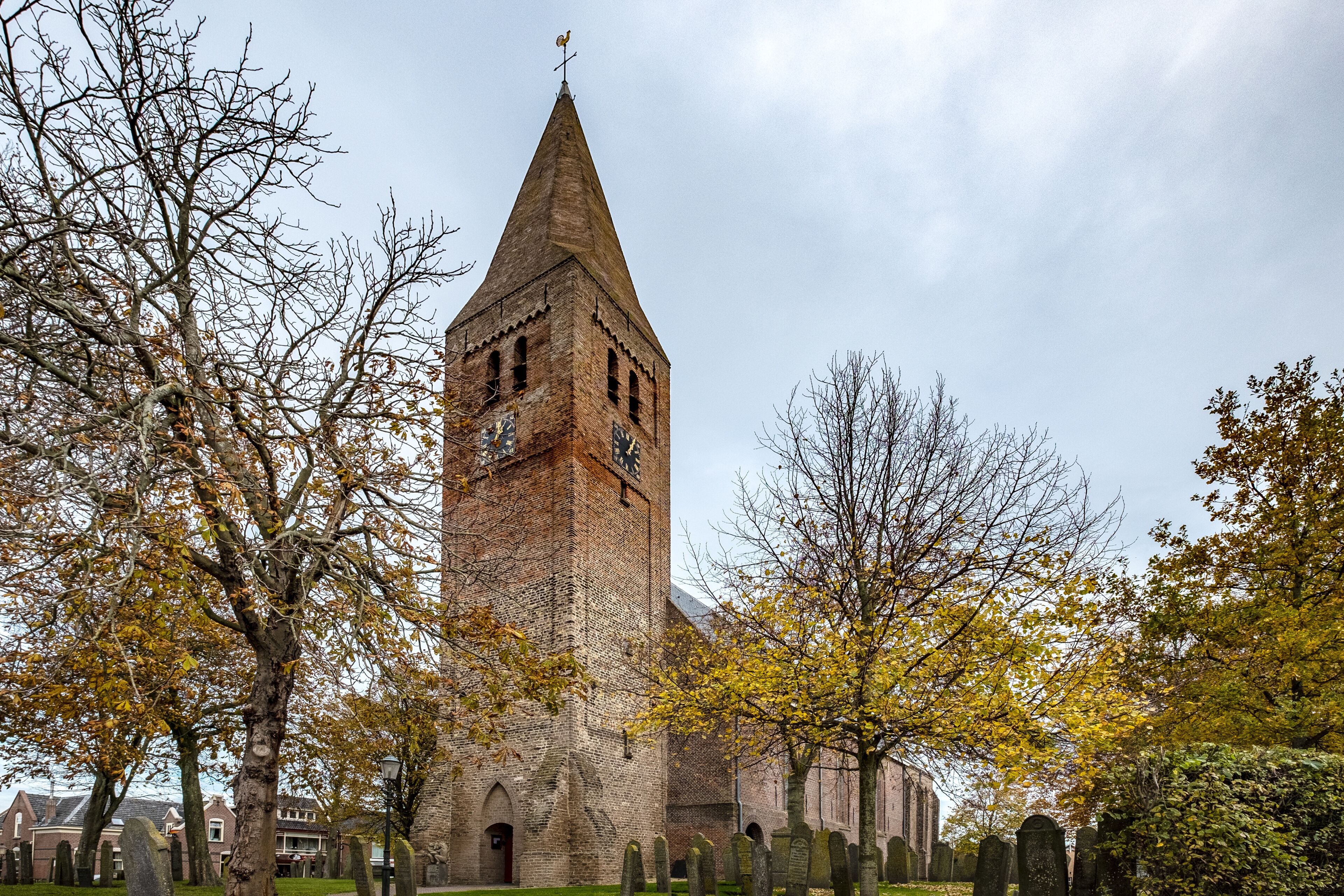A church with a tall tower, surrounded by trees and a cemetery.
