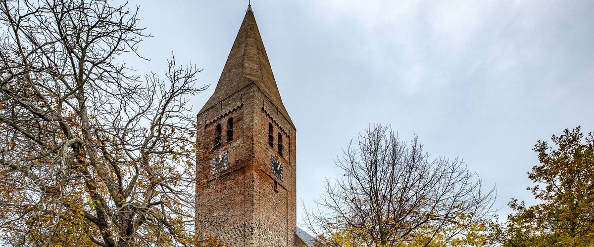 A church with a tall tower, surrounded by trees and a cemetery.