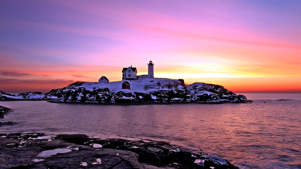 A lighthouse on a rocky island with a sunset sky.