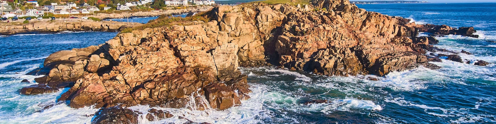 Huge rocky island with lighthouse on Maine coast aerial with waves crashing over rocks