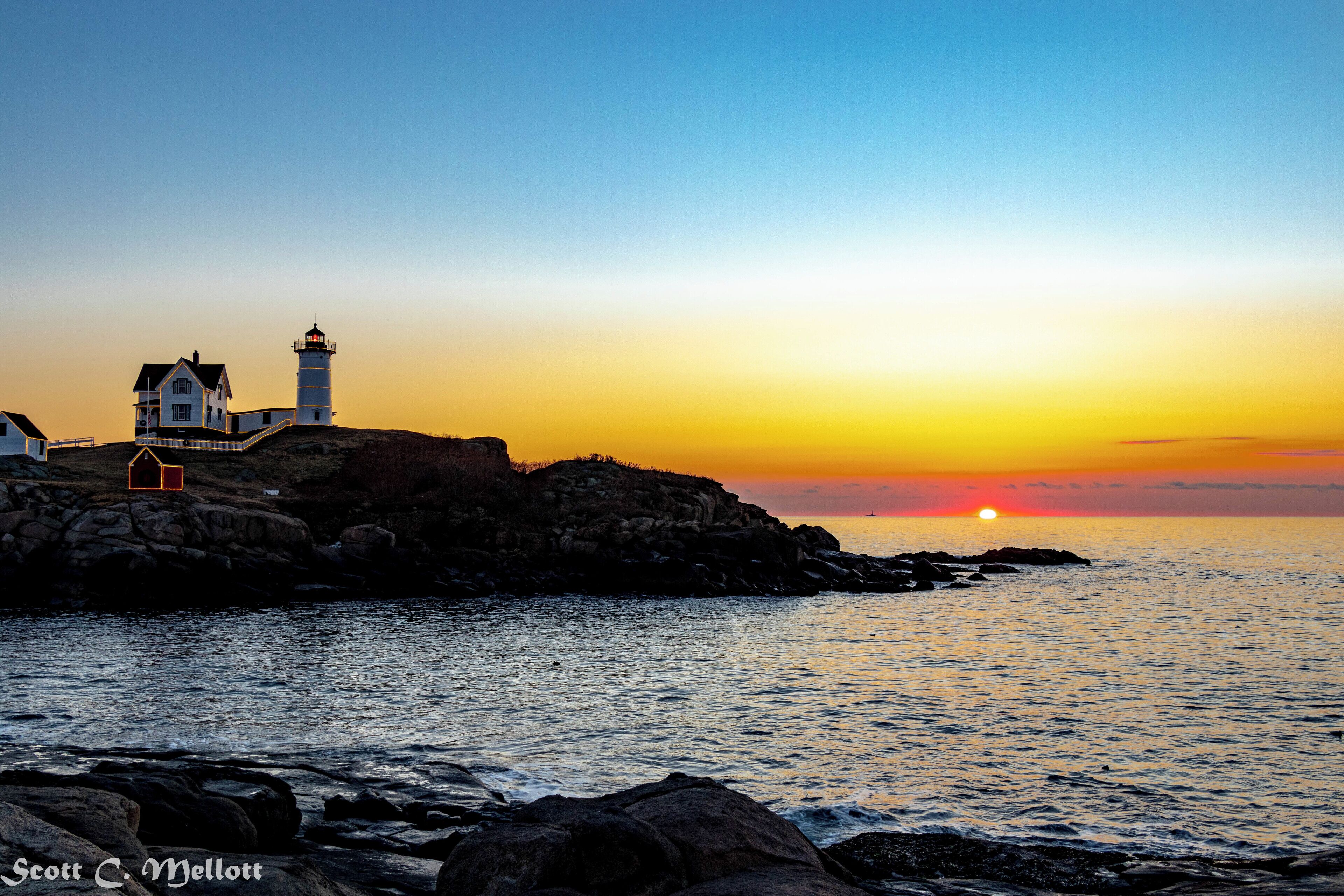 Sunrise at Nubble Lighthouse in York Beach, ME  The town puts Christmas lights on the buildings, fences and lighthouse structure during the Christmas season.  They are turned off just after dawn.

Camera info:
Canon 80D
Lens 18-135mm
Focal Length: 22mm
Exposure: 1/30 sec at f/9.0
ISO 100