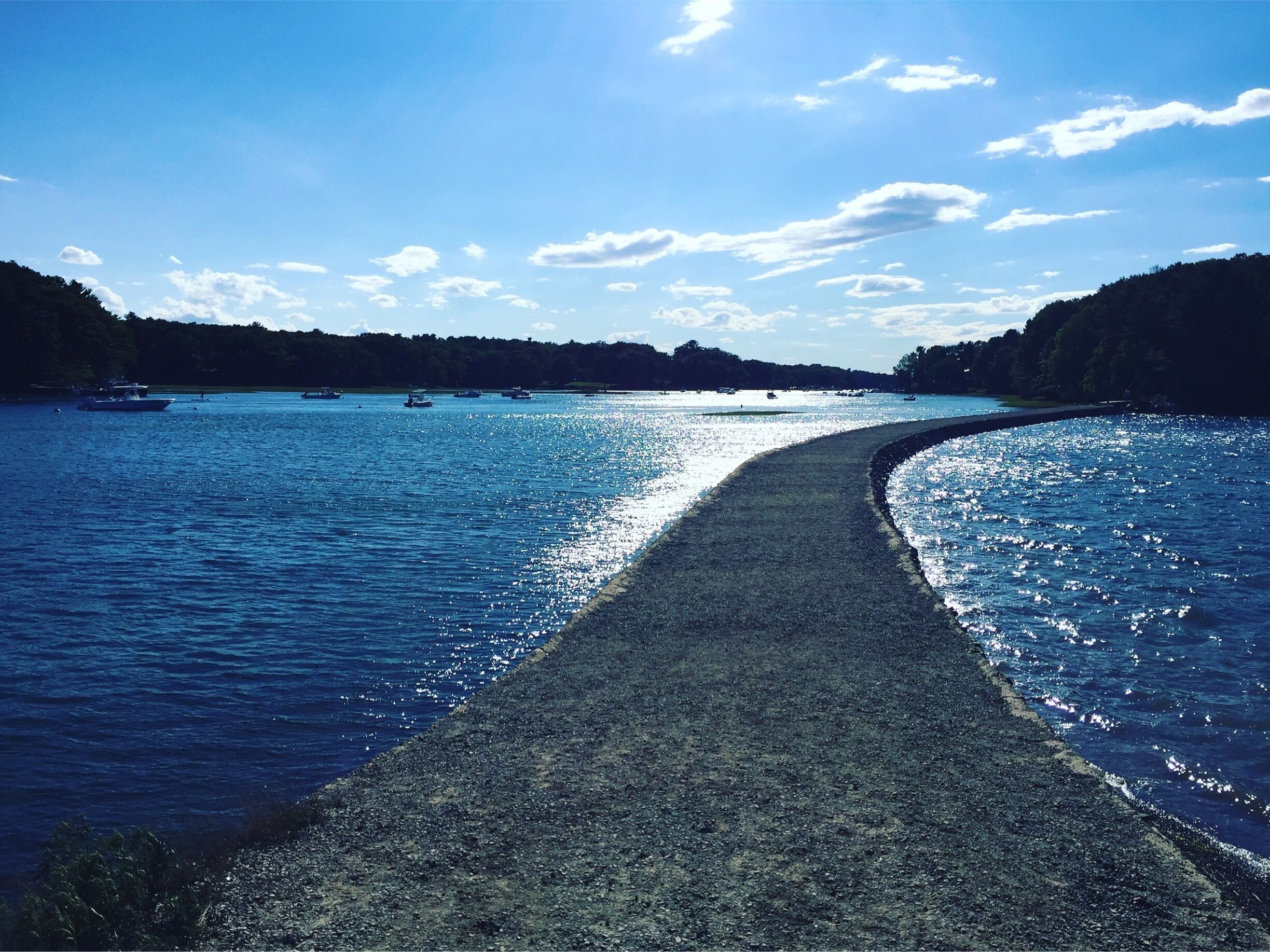 Un río con barcos, un sendero bordeado de piedras y colinas boscosas.