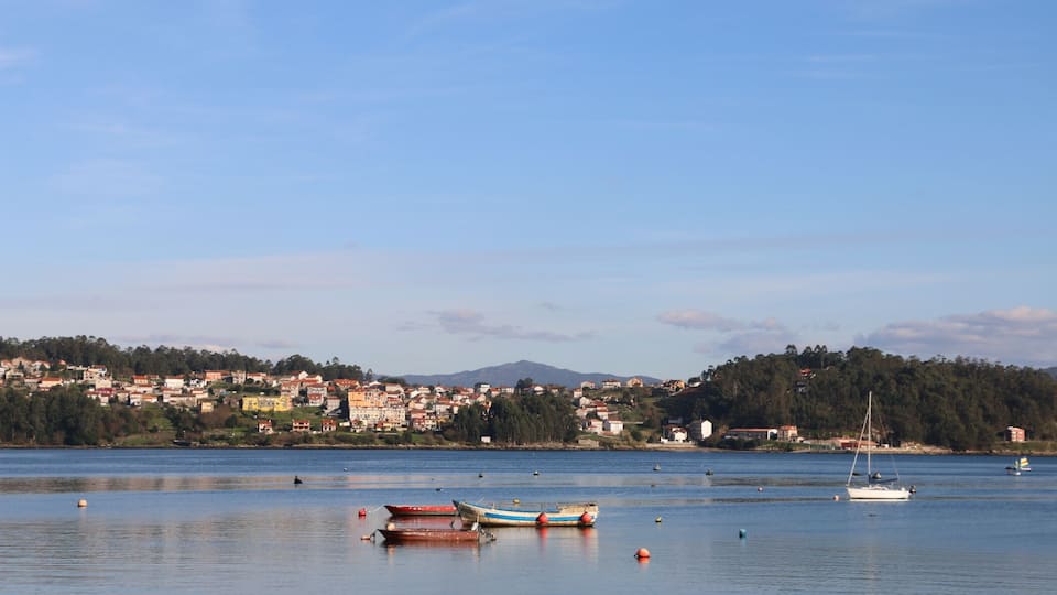 A calm lake with boats, a sailboat, and a town in the background.