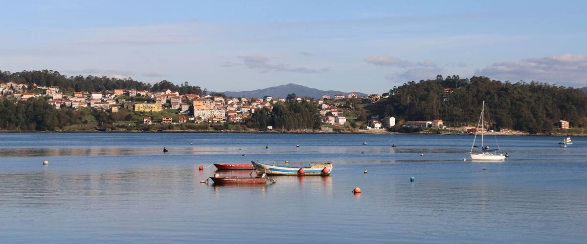 A calm lake with boats, a sailboat, and a town in the background.