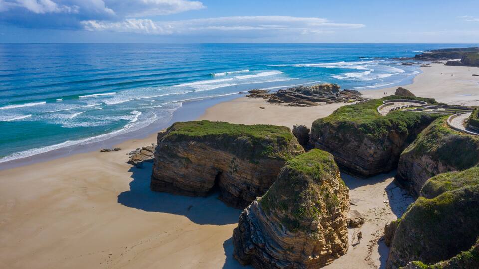 A coastal landscape with a sandy beach, rocky outcrops, and the ocean.