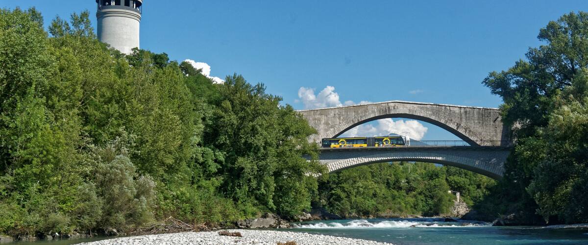 A stone bridge over a river, a lighthouse, and dense green trees.