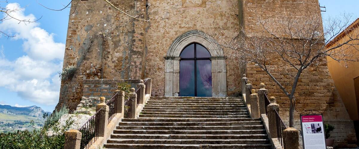 A historic church with a bell tower, a staircase leading up to the entrance, and a clear blue sky in the background.